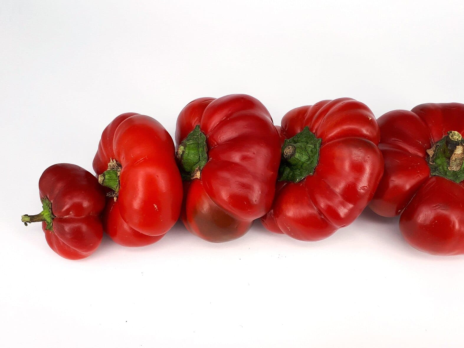 Five fresh red capsicum (bell peppers) in a row on a white background