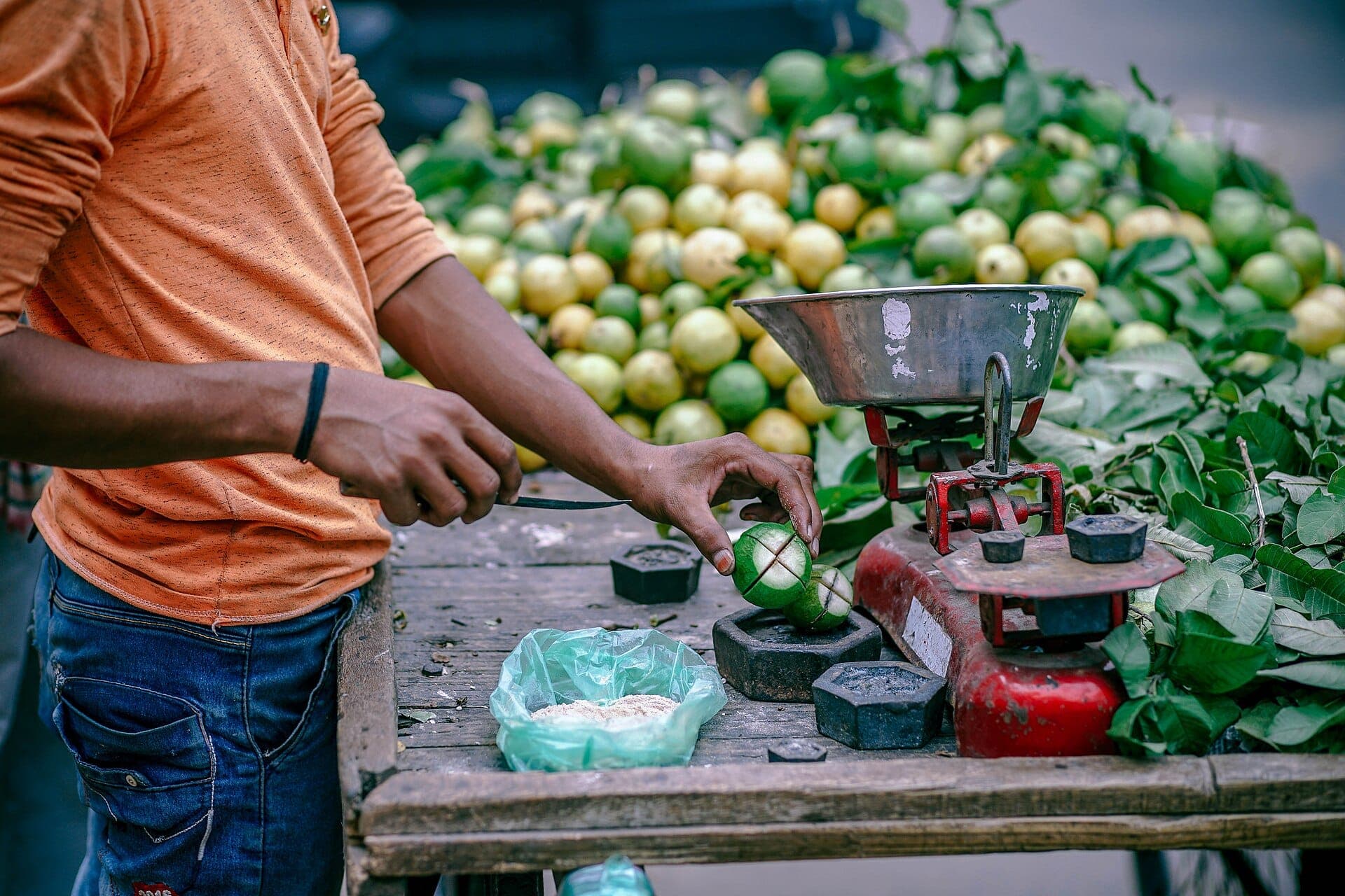 A produce seller weighing fresh limes on a scale at a street stall